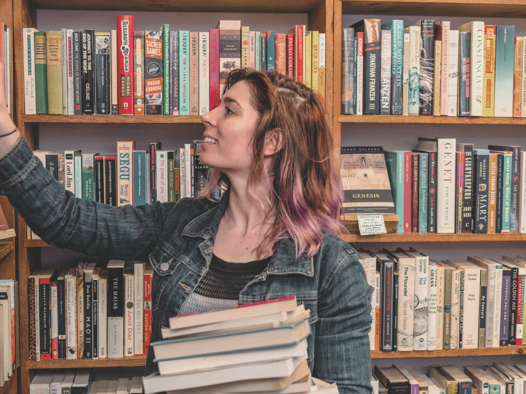 woman browsing book shelves and holding a stack of books