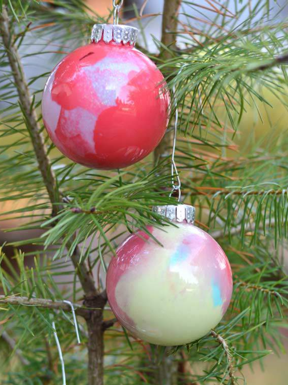 Two colorful Christmas ornaments hanging on a pine tree.