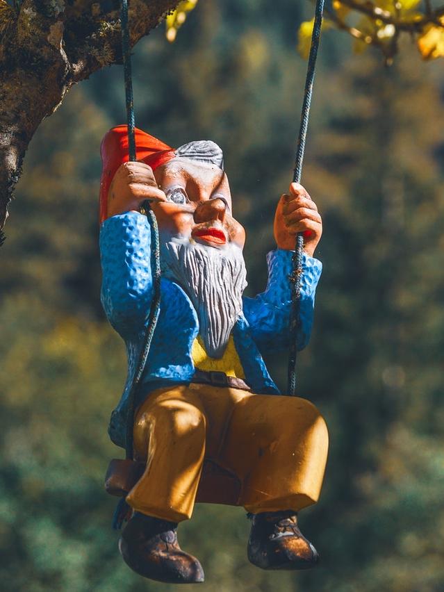 image of a gnome statue sitting on a swing chair hanging from a tree