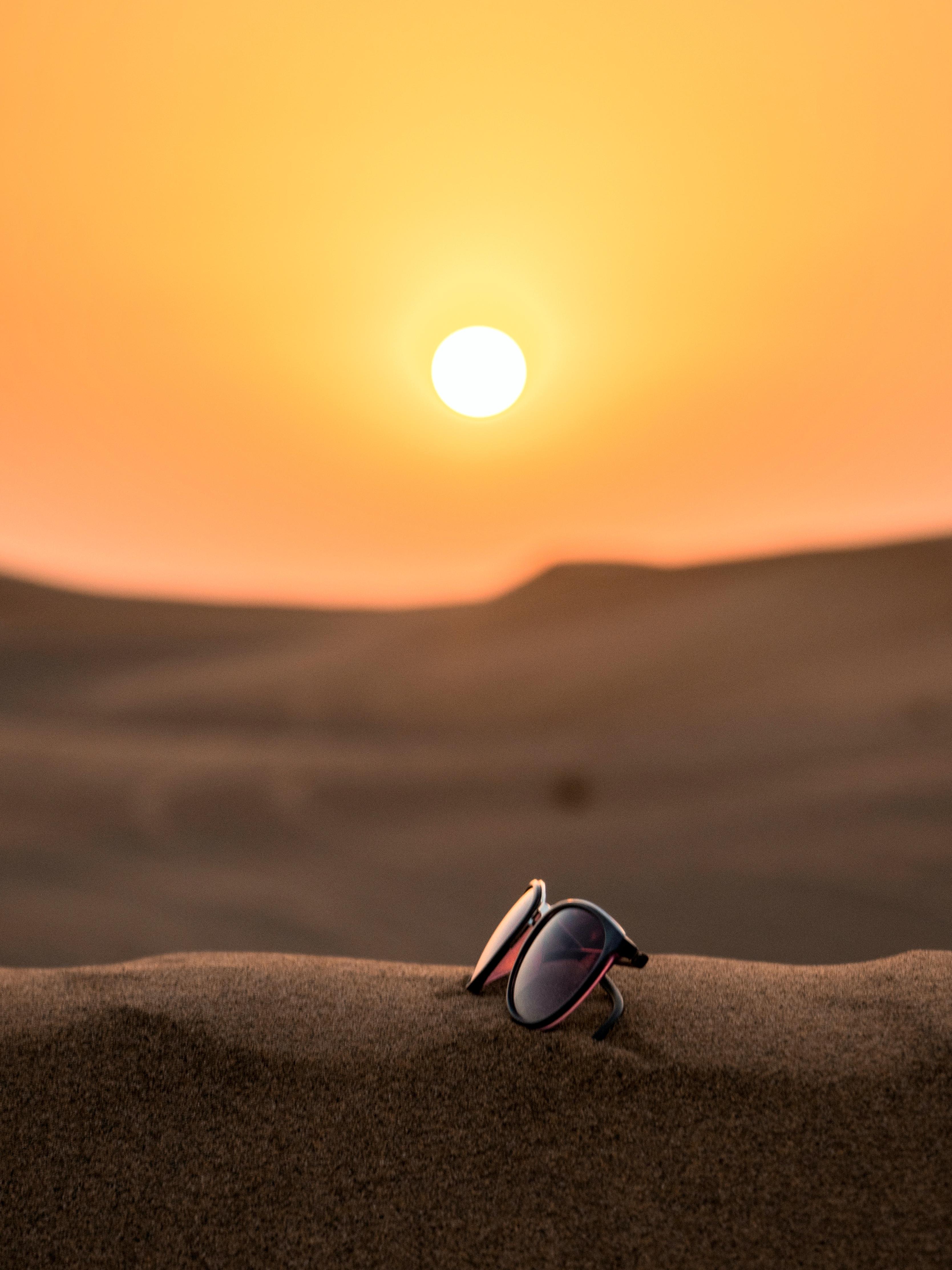 photo of the sun and sunglasses on top of sand