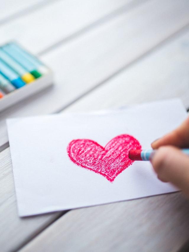 person drawing a heart on paper with crayons