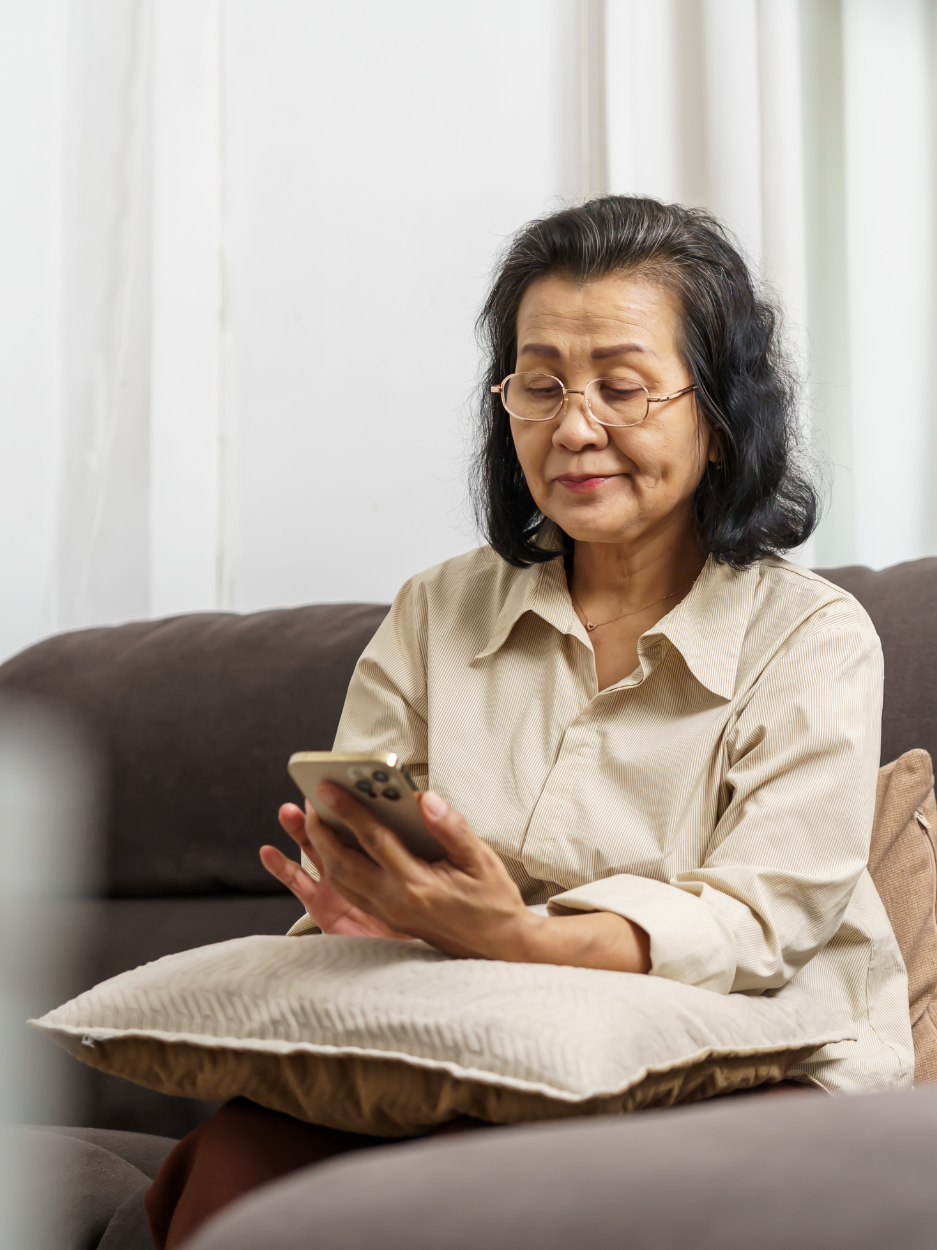 Older woman using smartphone on couch.