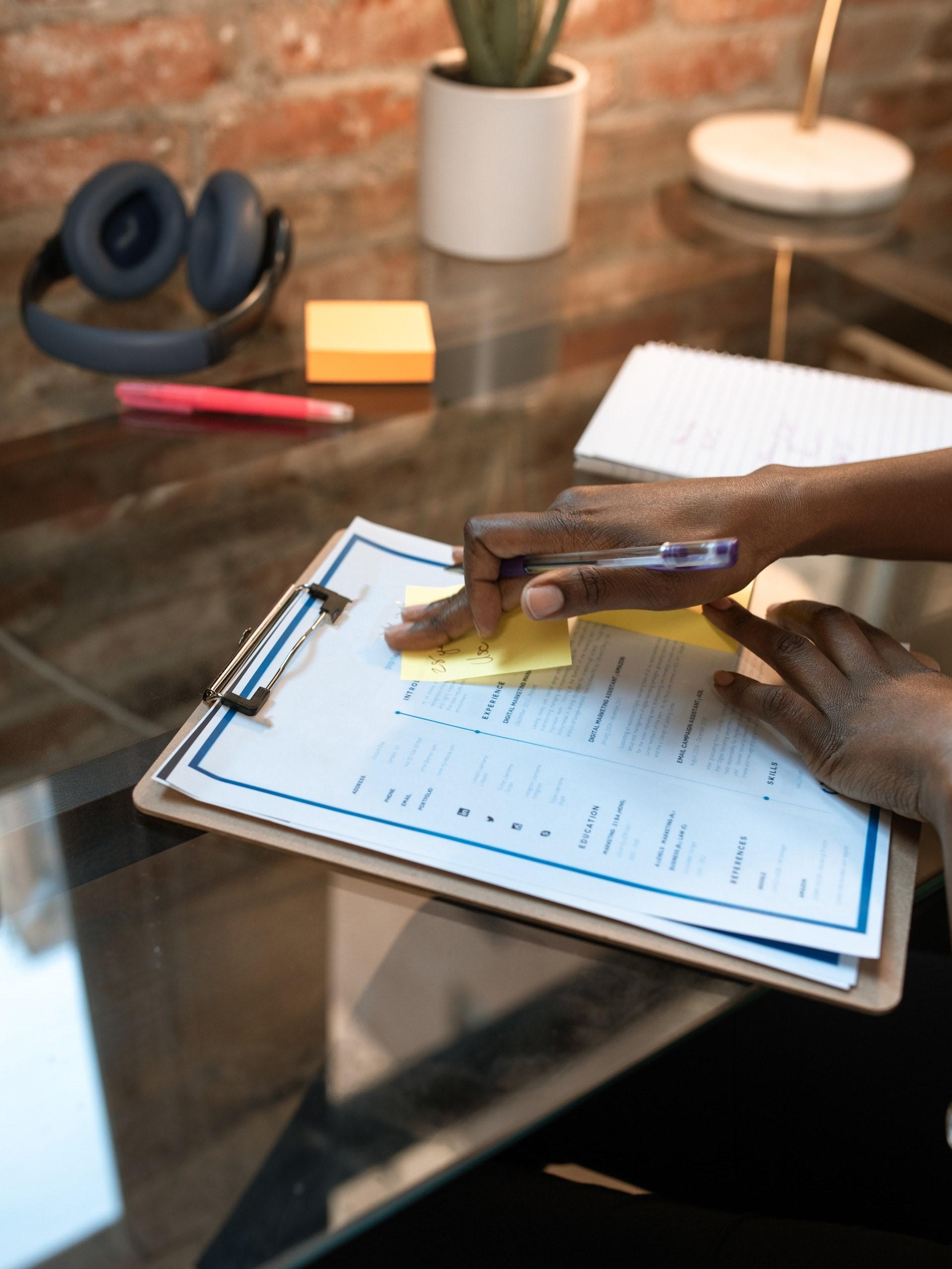 photo of a resume attached to a clipboard on a desk with a persons hands